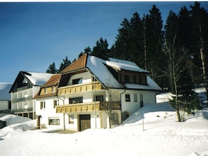 A multi-story chalet with a balcony, surrounded by snow and trees.
