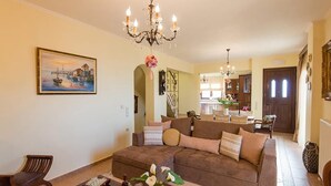 A living room with a brown sofa, a wooden coffee table, and a chandelier. - Νikolaos Villa with Private Pool, Playground & BBQ (Rethymno)