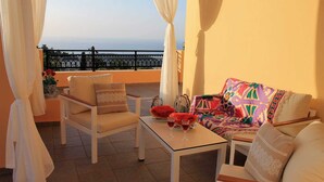A balcony with a white table, two white chairs, a colorful sofa, and a view of the sea. - Νikolaos Villa with Private Pool, Playground & BBQ (Rethymno)