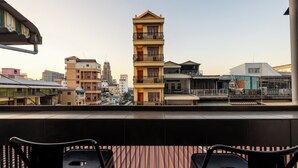 A balcony with two black chairs, overlooking a cityscape with various buildings, including a prominent yellow building with balconies. - Lofty Comfort Stay-Relax by Soben Home (Phnom Penh)