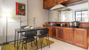 A compact kitchen with wooden cabinets, a black dining table with two chairs, a gas stove, and a window providing natural light. - Lofty Comfort Stay-Relax by Soben Home (Phnom Penh)