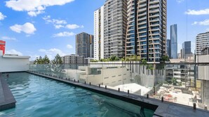 A rooftop swimming pool with a glass barrier, surrounded by high-rise buildings and a clear sky. - Unbeatable River & CBD Views Pool/2Car/Prime Spot (South Brisbane)