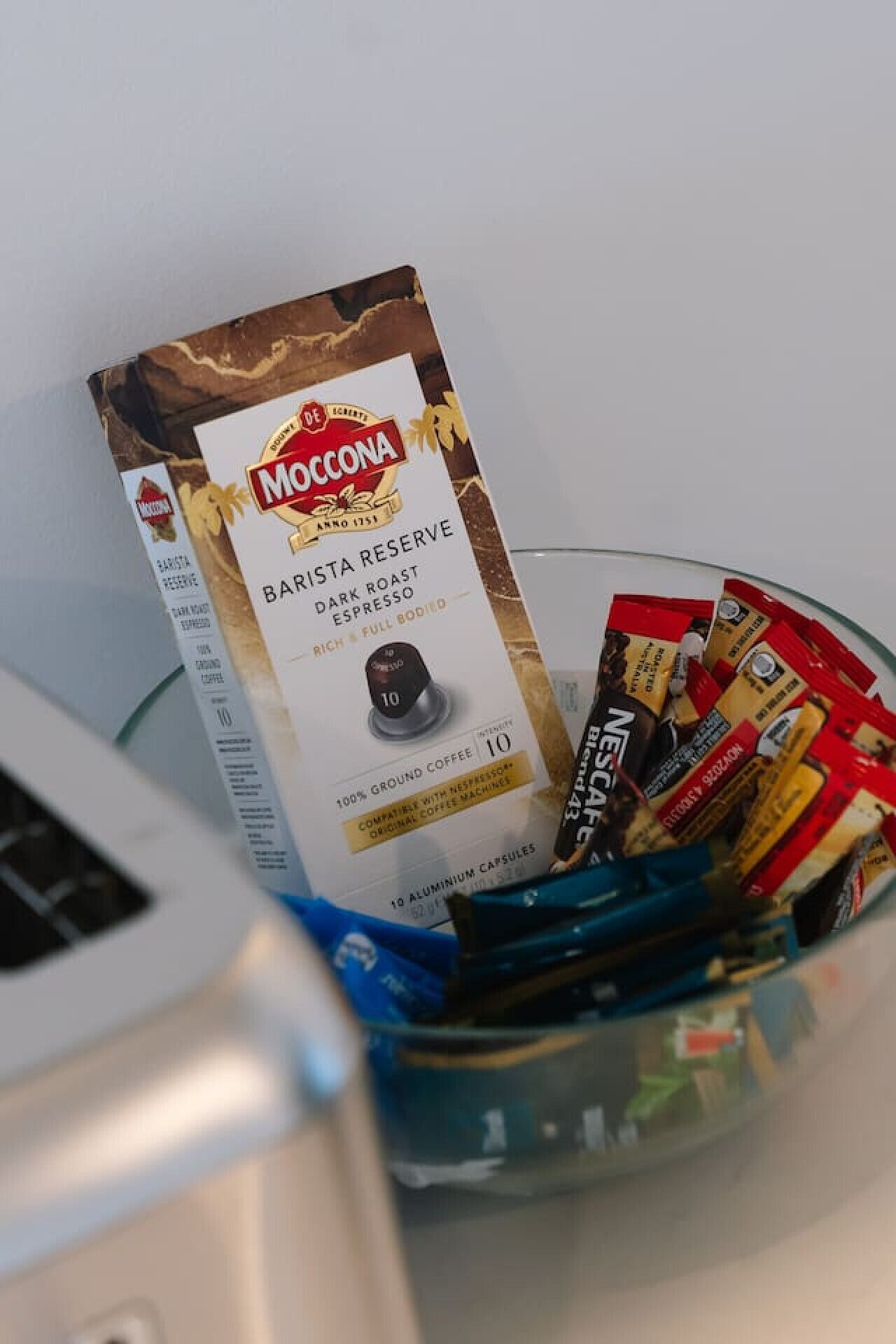 A glass container filled with coffee pods and a box of Moccona Barista Reserve coffee.
