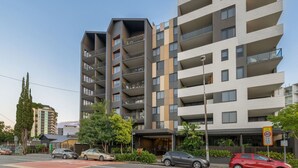 Een modern meerlaags appartementencomplex met balkons, een straatbeeld en geparkeerde auto's.