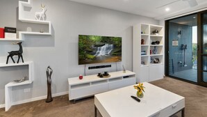 Een moderne woonkamer met een flatscreen televisie, witte schapenkasten en een glazen deur die leidt naar een buitenruimte.