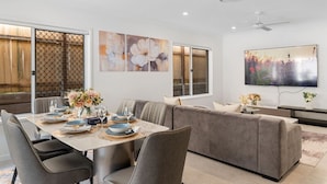 Un espace de repas moderne avec une table dressée pour quatre personnes, un canapé gris et un téléviseur fixé au mur.