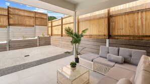 Un espace de vie extérieur moderne avec une table basse en verre, un canapé beige et une plante en pot.