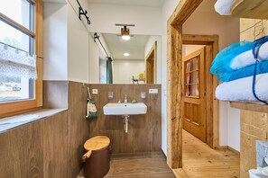 A narrow bathroom with wooden walls, a sink, a toilet, and a window. - Holiday Home Edt (Bad Goisern)