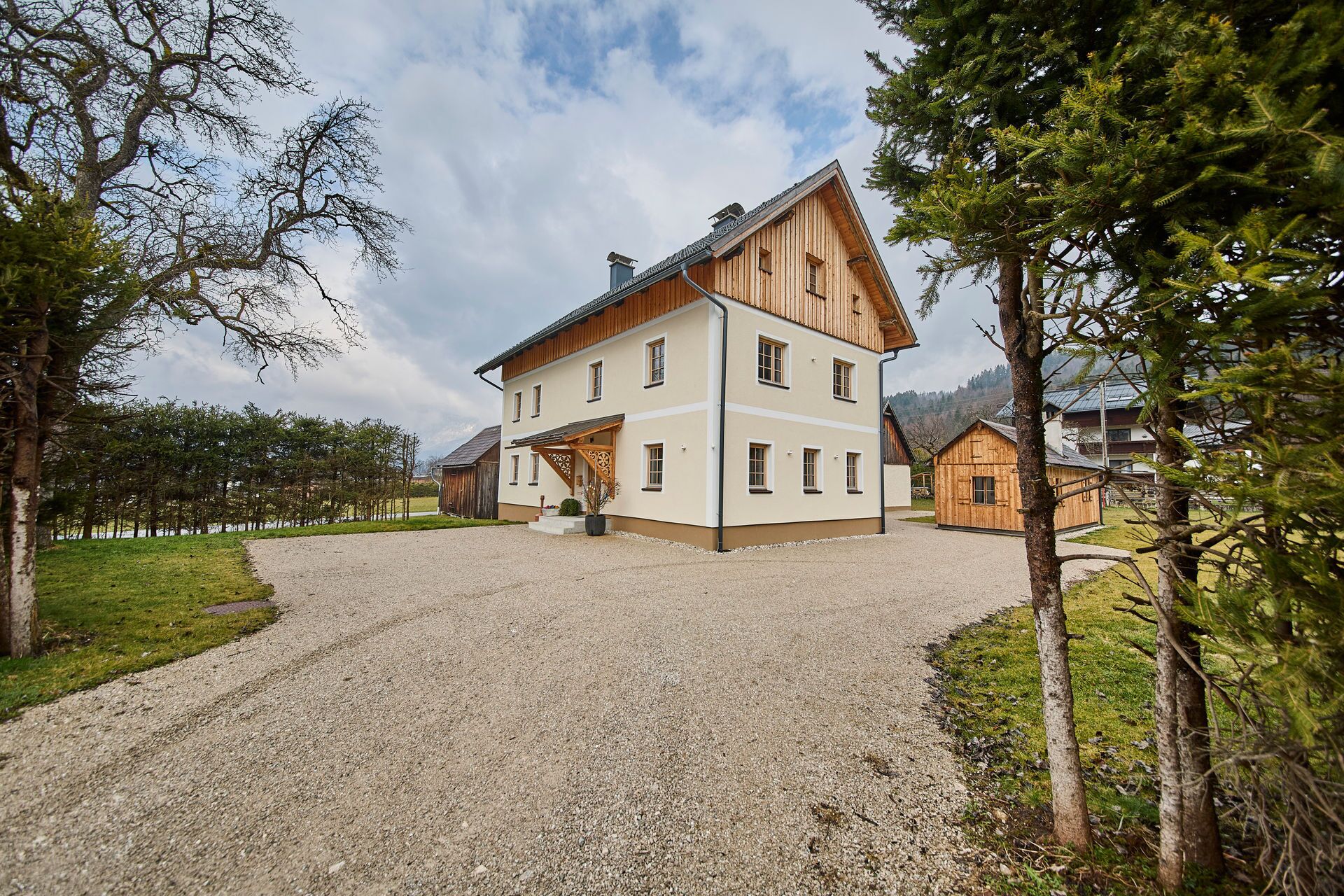 A large, two-story wooden house with a gravel driveway and surrounding trees.