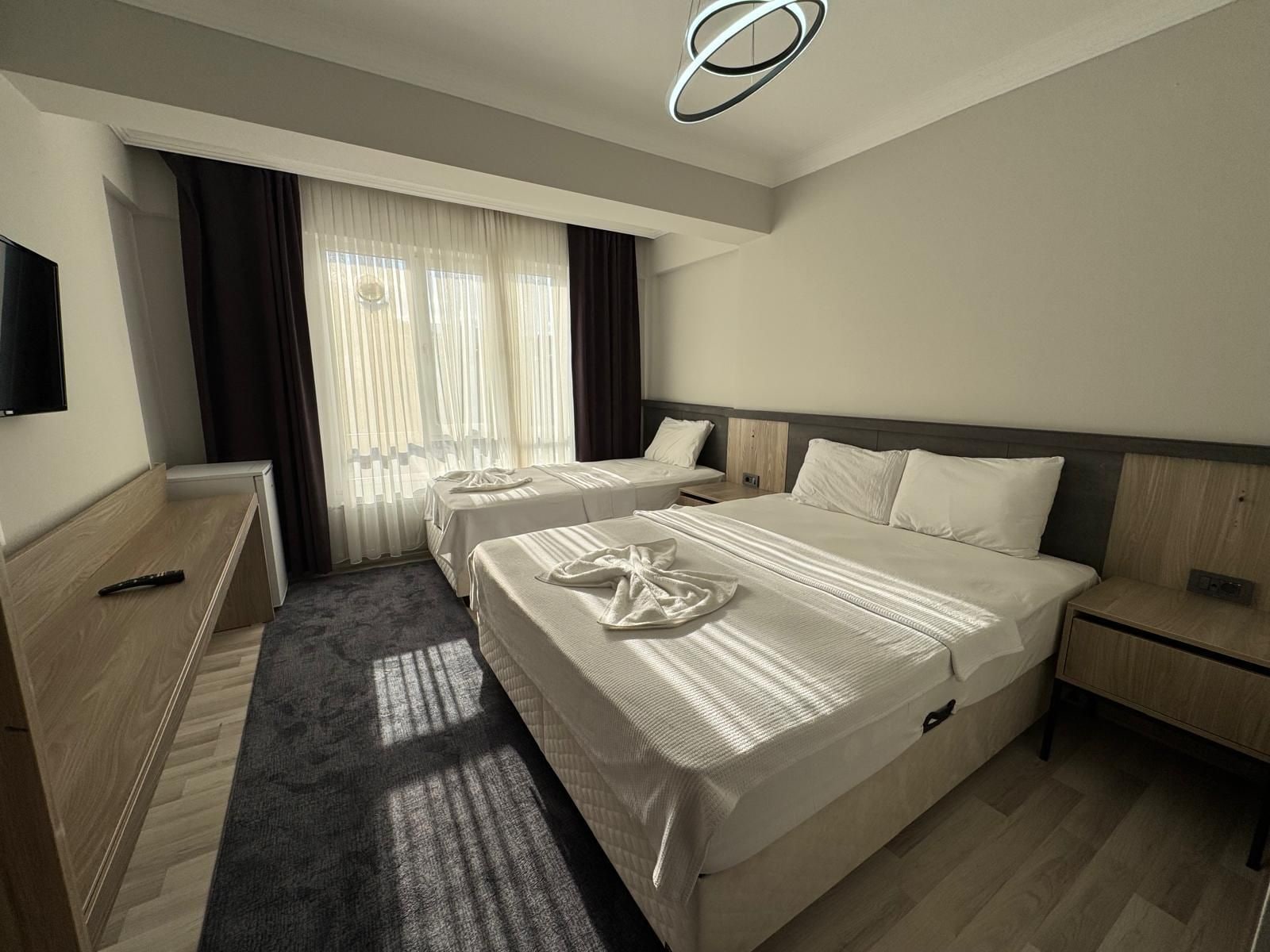 Ein Hotelzimmer mit zwei Betten, einem Flachbildfernseher, einem Schreibtisch und einem großen Fenster mit Vorhängen.