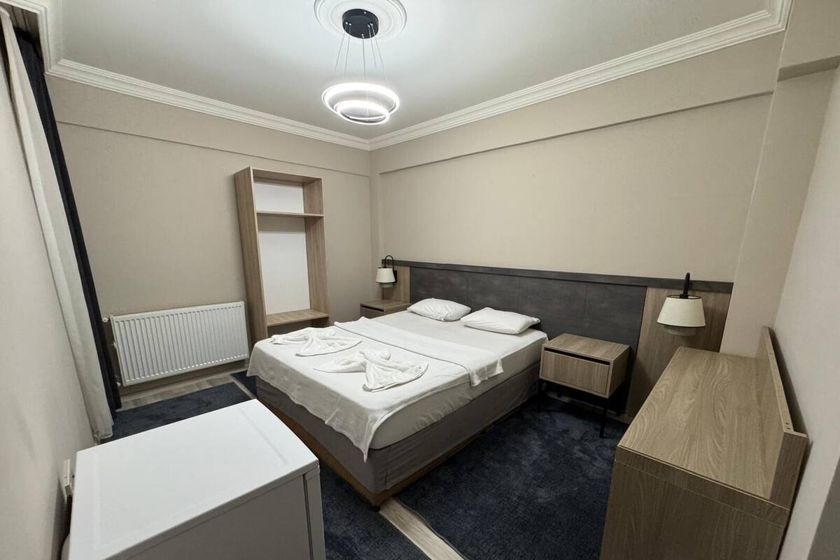 Een hotelkamer met een bed, nachtkastjes, een garderobe, een radiator en een plafondlamp.