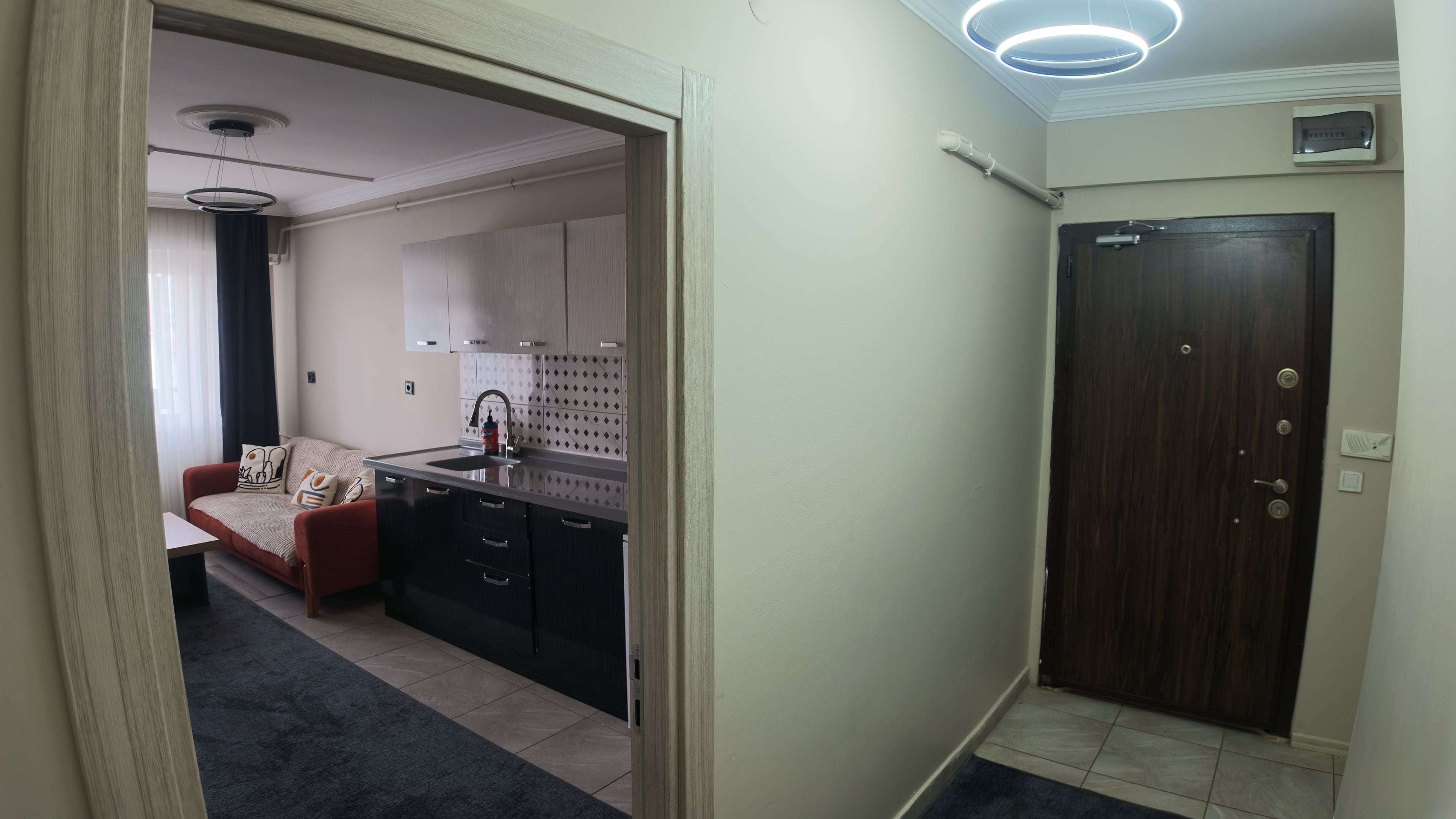 Una cocina compacta con electrodomésticos modernos, una puerta de madera oscura y un sofá rojo en la sala contigua.