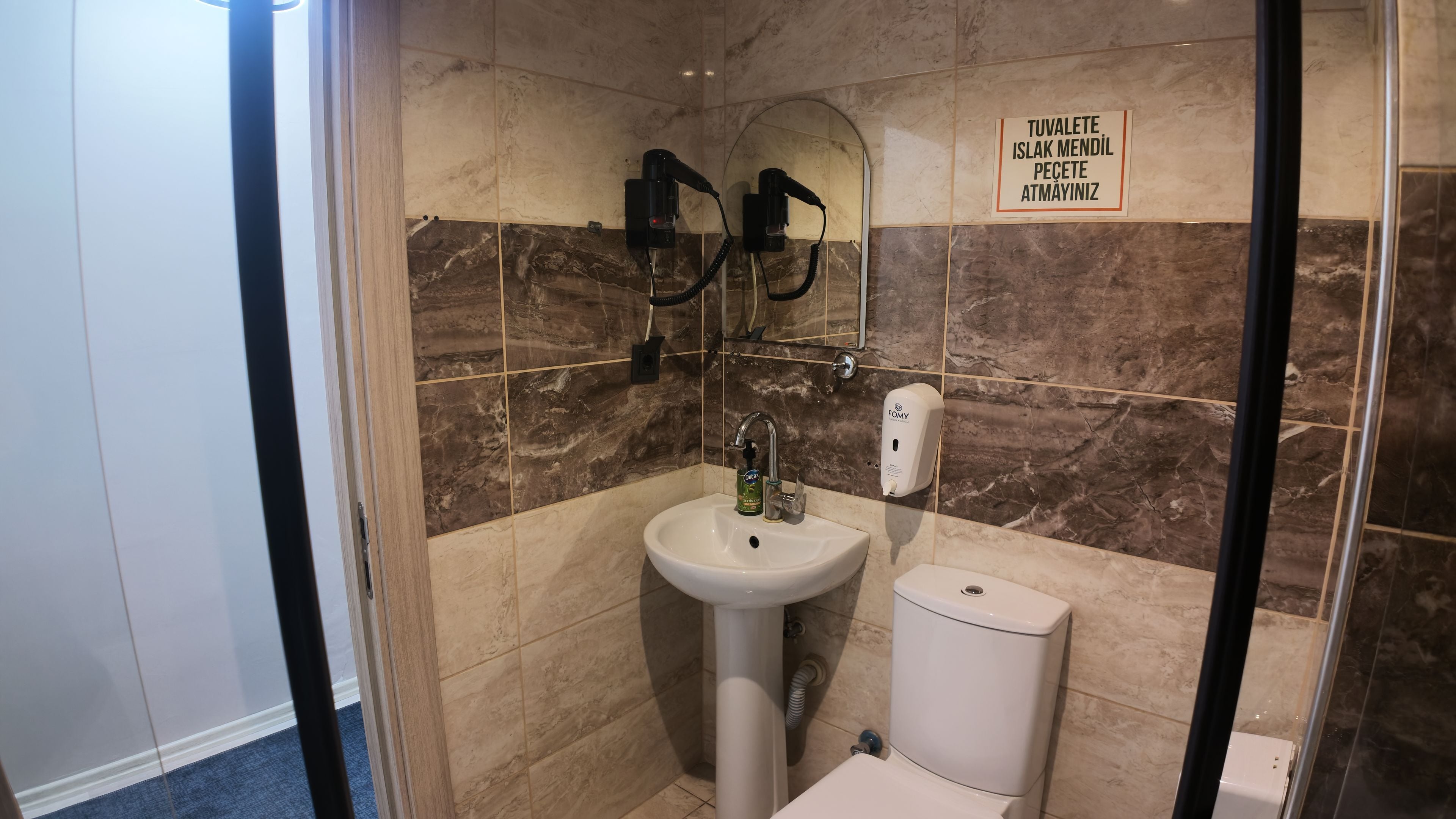 A bathroom with a sink, a mirror, and a sign indicating the availability of a towel and a hand dryer.