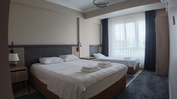 Habitación de hotel con dos camas, una mesita de noche, una lámpara y vistas al exterior a través de una ventana.