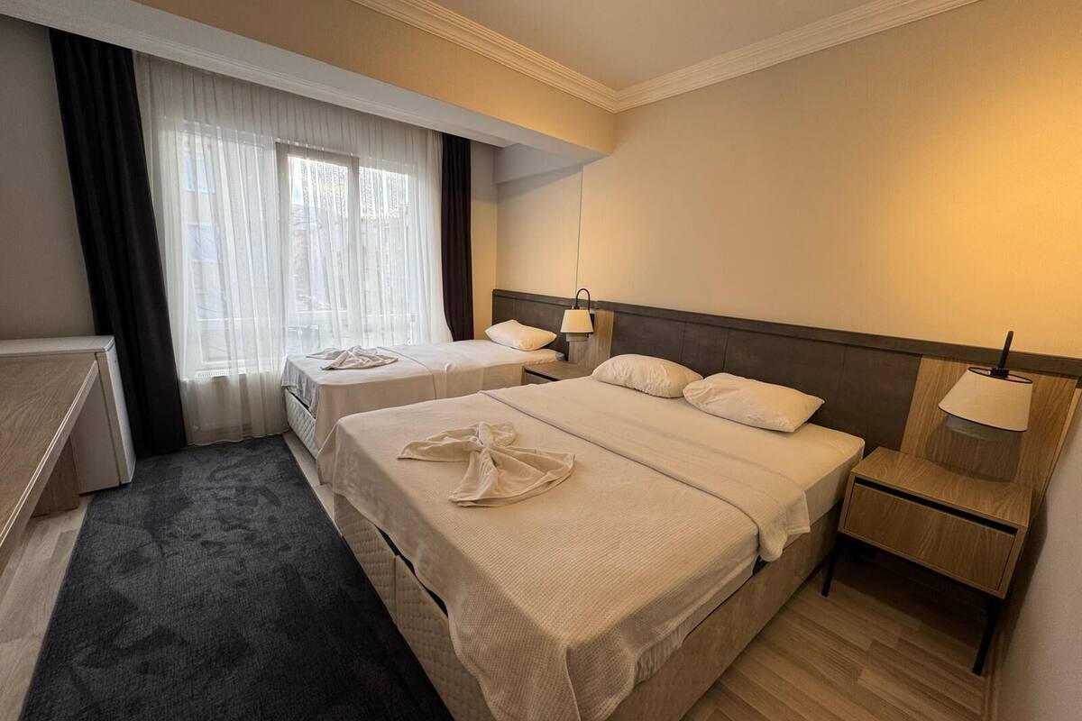 Een hotelkamer met twee bedden, een bureau, een stoel, een nachtkastje met een lamp en een raam met dunne gordijnen.
