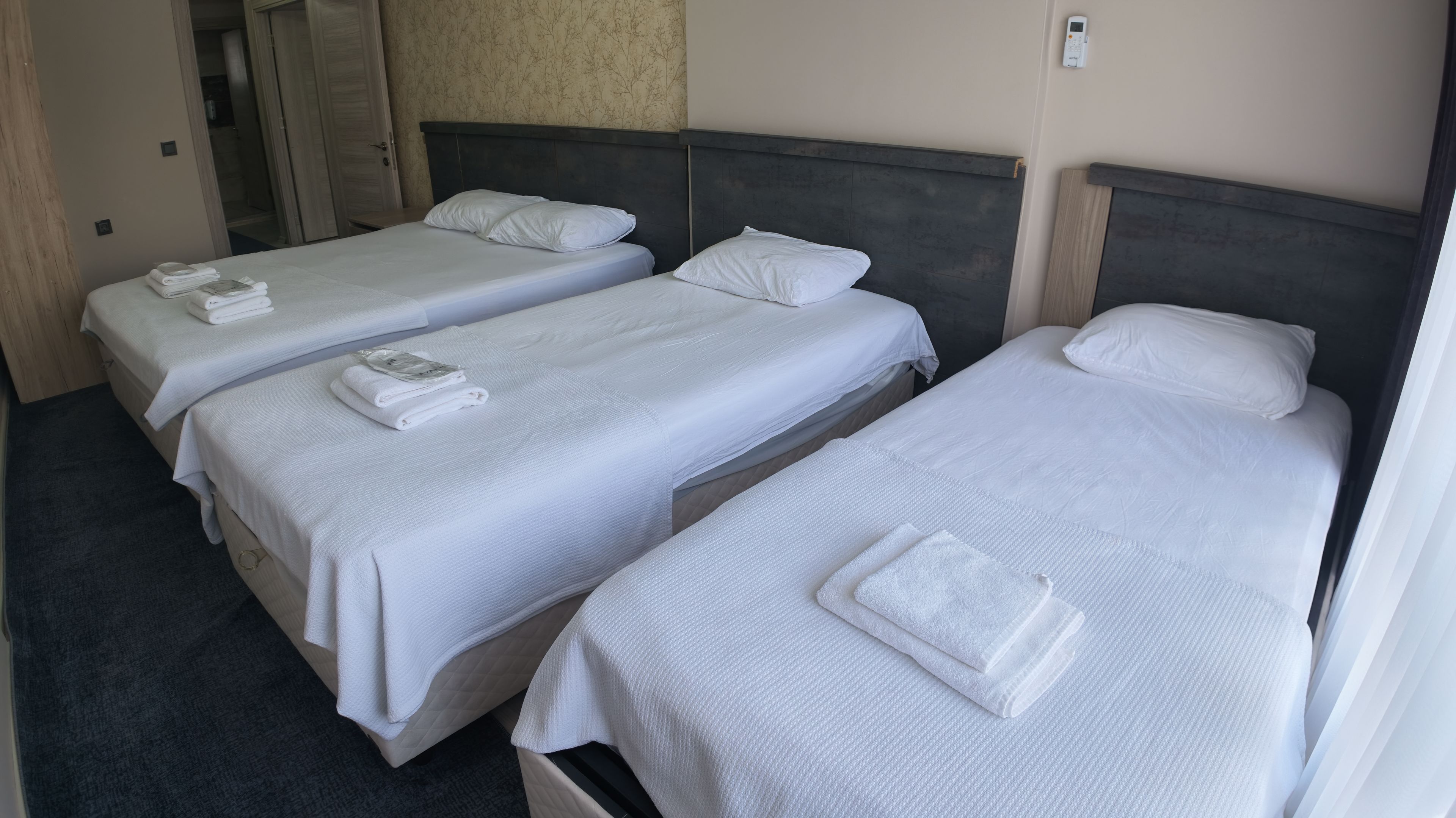 A hotel room with three single beds, each with white linens and pillows, and a bedside table with a phone.