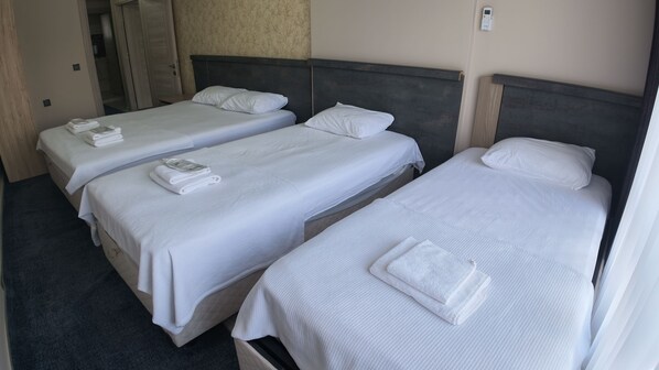 Habitación de hotel con tres camas individuales, cada una con ropa blanca y almohadas, y una mesita de noche con teléfono.