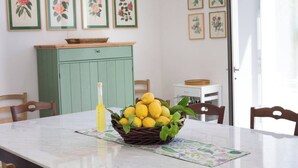 Una mesa de comedor con una cesta de limones y una botella de aceite de oliva, rodeada de sillas y decorada con cuadros de flores en las paredes.