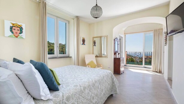 Un dormitorio con una cama grande, una silla, un aparador y un balcón con vistas.