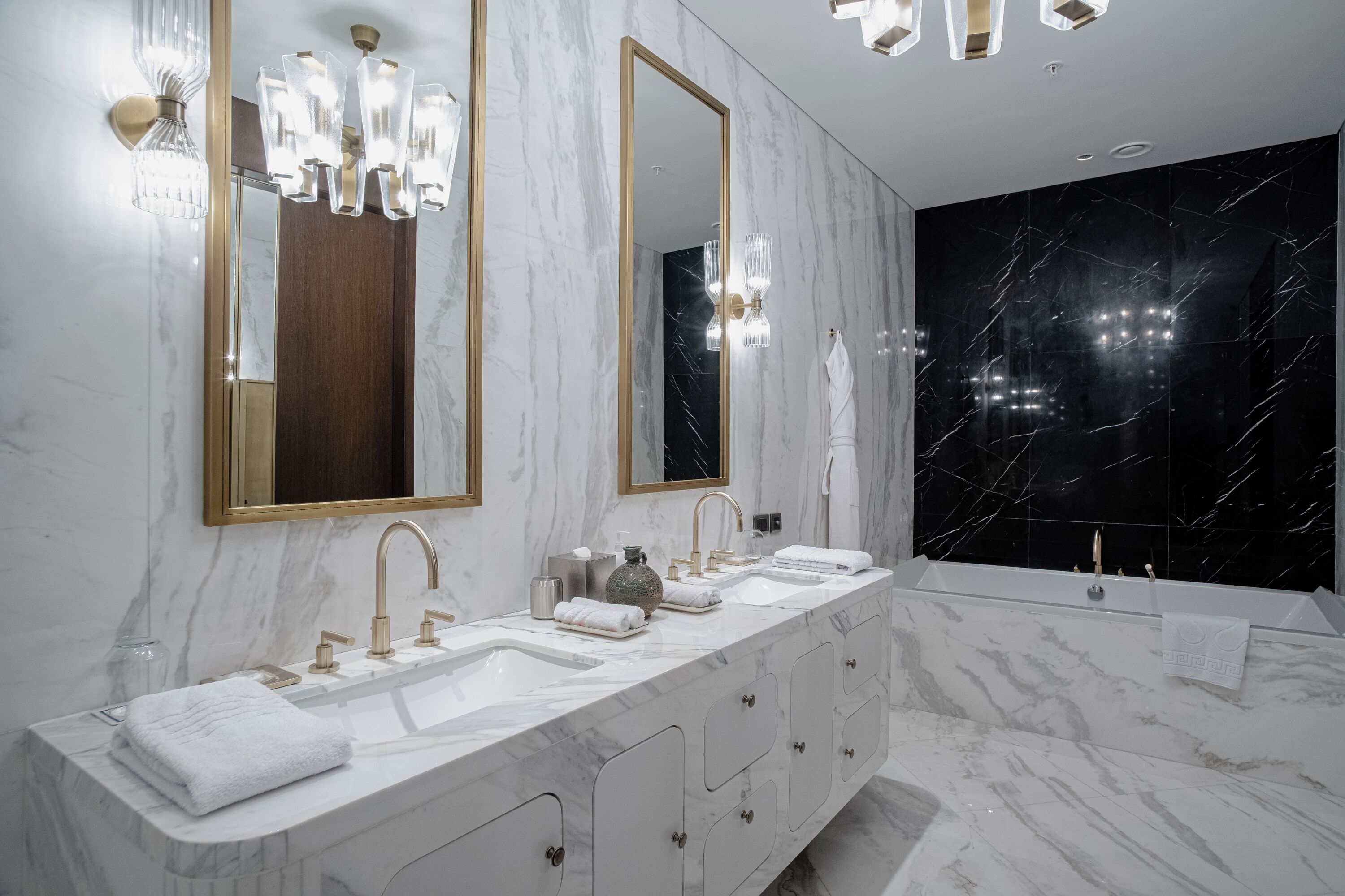 A modern bathroom with a large mirror, two sinks, a bathtub, and marble walls.
