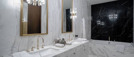 A modern bathroom with a large mirror, two sinks, a bathtub, and marble walls.