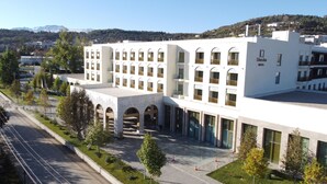A modern hotel with a central courtyard, multiple floors, and a view of the surrounding area including trees and distant buildings.
