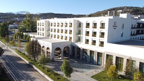 A modern hotel with a central courtyard, multiple floors, and a view of the surrounding area including trees and distant buildings.
