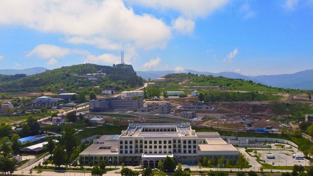 A large building with a central courtyard, surrounded by greenery and a hilly landscape.