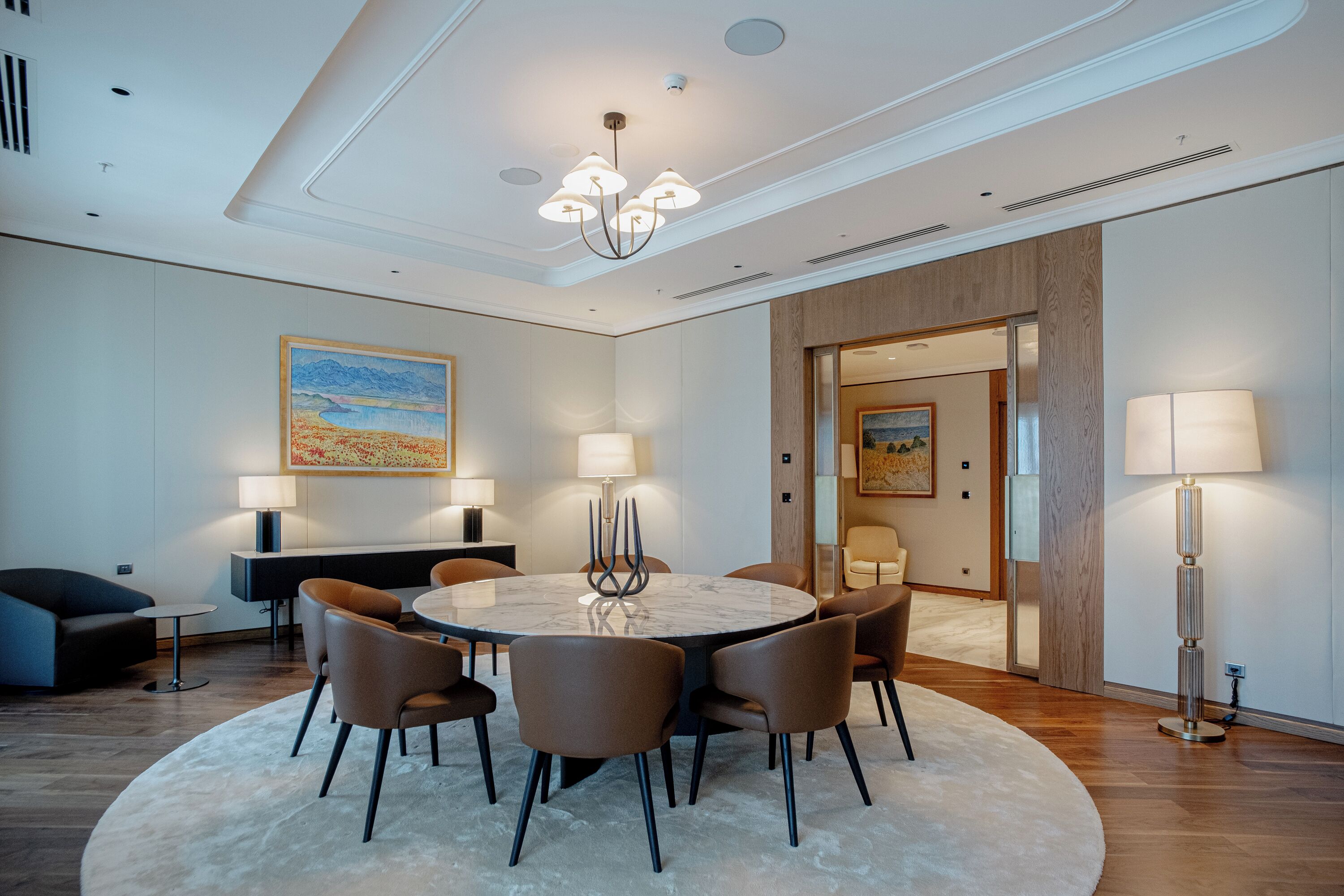 A modern dining area with a round table, brown chairs, and a central light fixture.