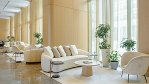 A spacious lobby with a modern white sofa, armchairs, and a coffee table. There are potted plants and a large window providing natural light. - Shusha Hotel & Conference Center (Shusha)