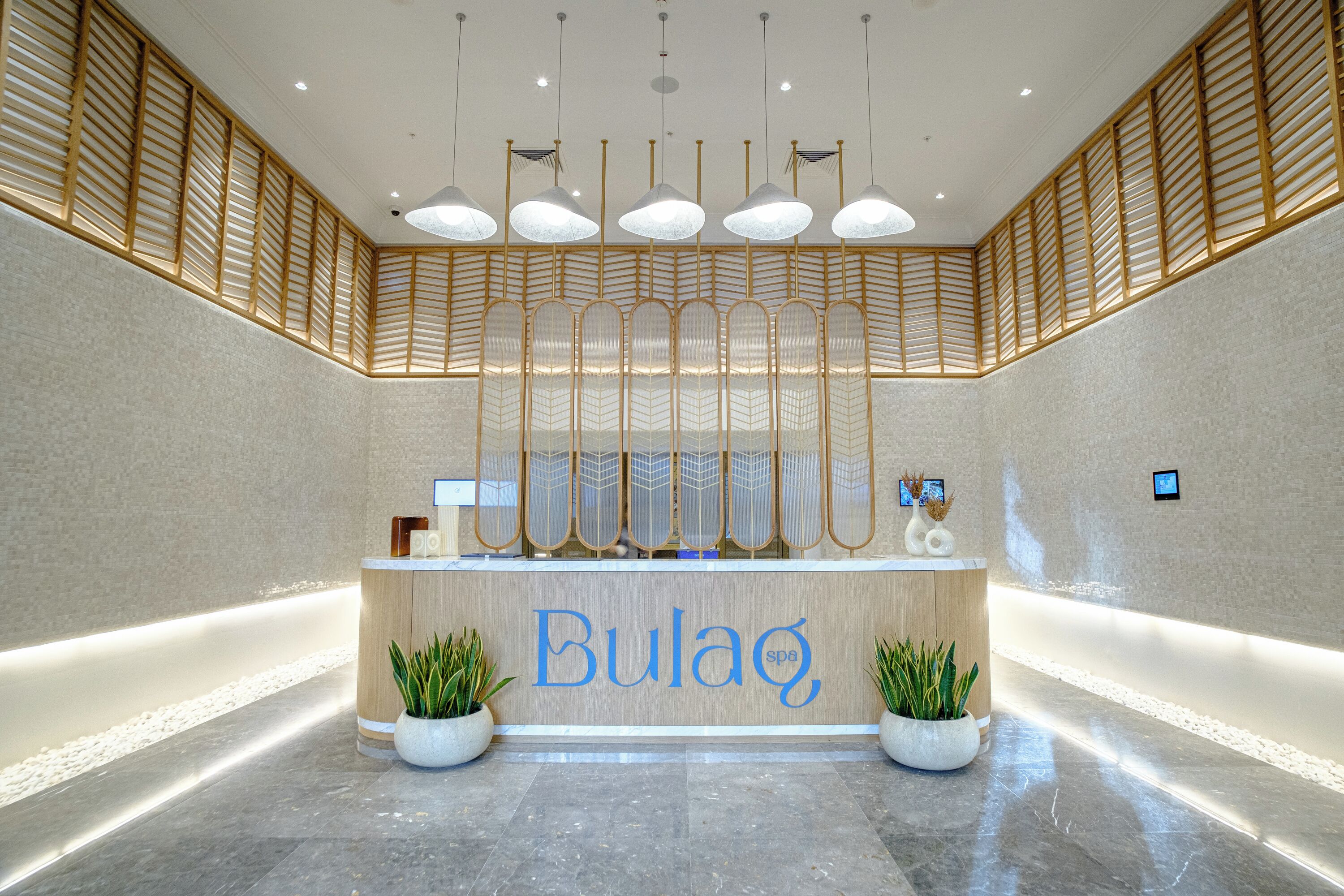 Een receptie met een houten balie, potplanten en een bord waarop 'Bulaq spa' staat.