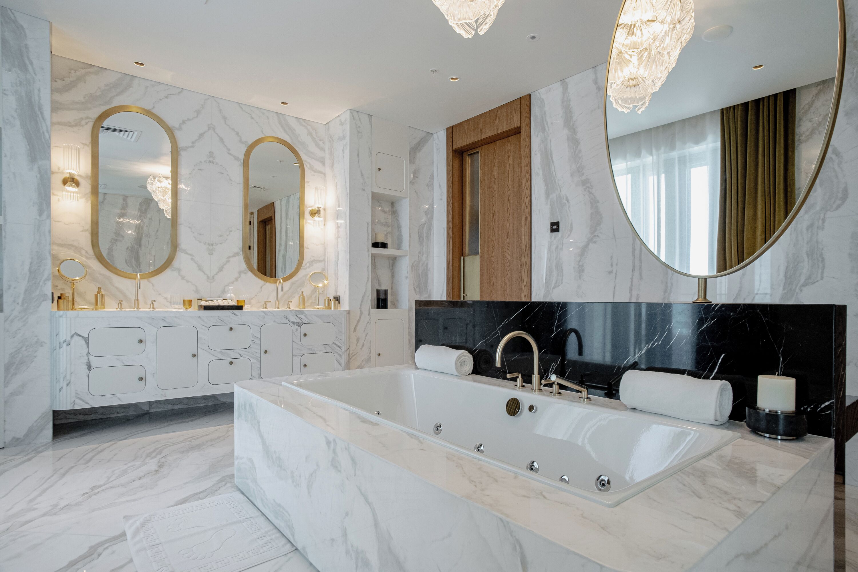 Un baño moderno con una bañera grande, paredes de mármol y dos espejos amplios.