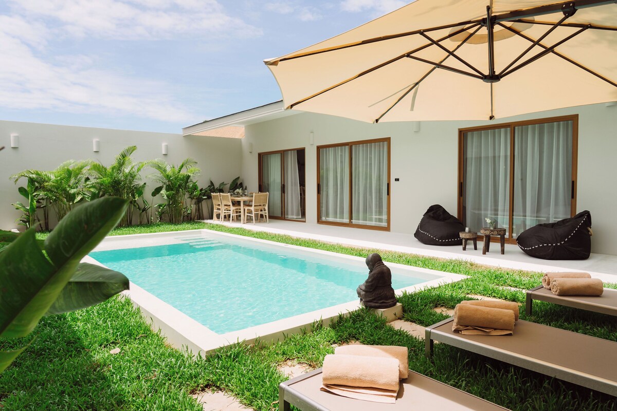 A pool area with lounge chairs, a statue, and a large umbrella.
