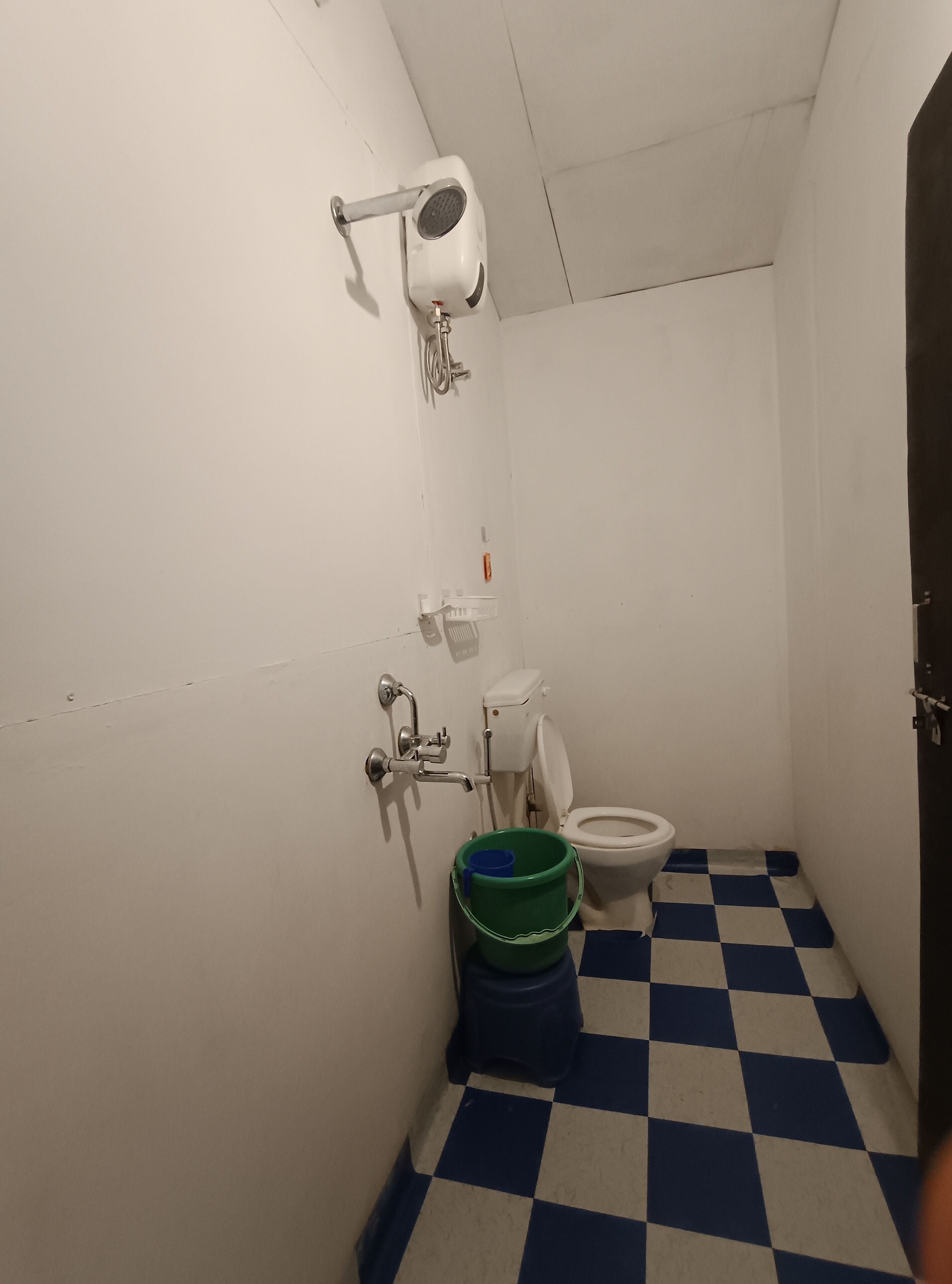 Ein kleines Badezimmer mit Toilette, einer an der Wand befestigten Duschbrause und einem grünen Eimer auf dem Boden.