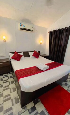 A hotel room with a bed, a red throw, a white pillow, a black headboard, a wall-mounted air conditioner, and a checkered floor. - Love paradise  (Arambol)