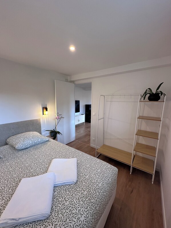 A modern bedroom with a large bed, a bedside table with a lamp, a wardrobe, and a small plant on a shelf.