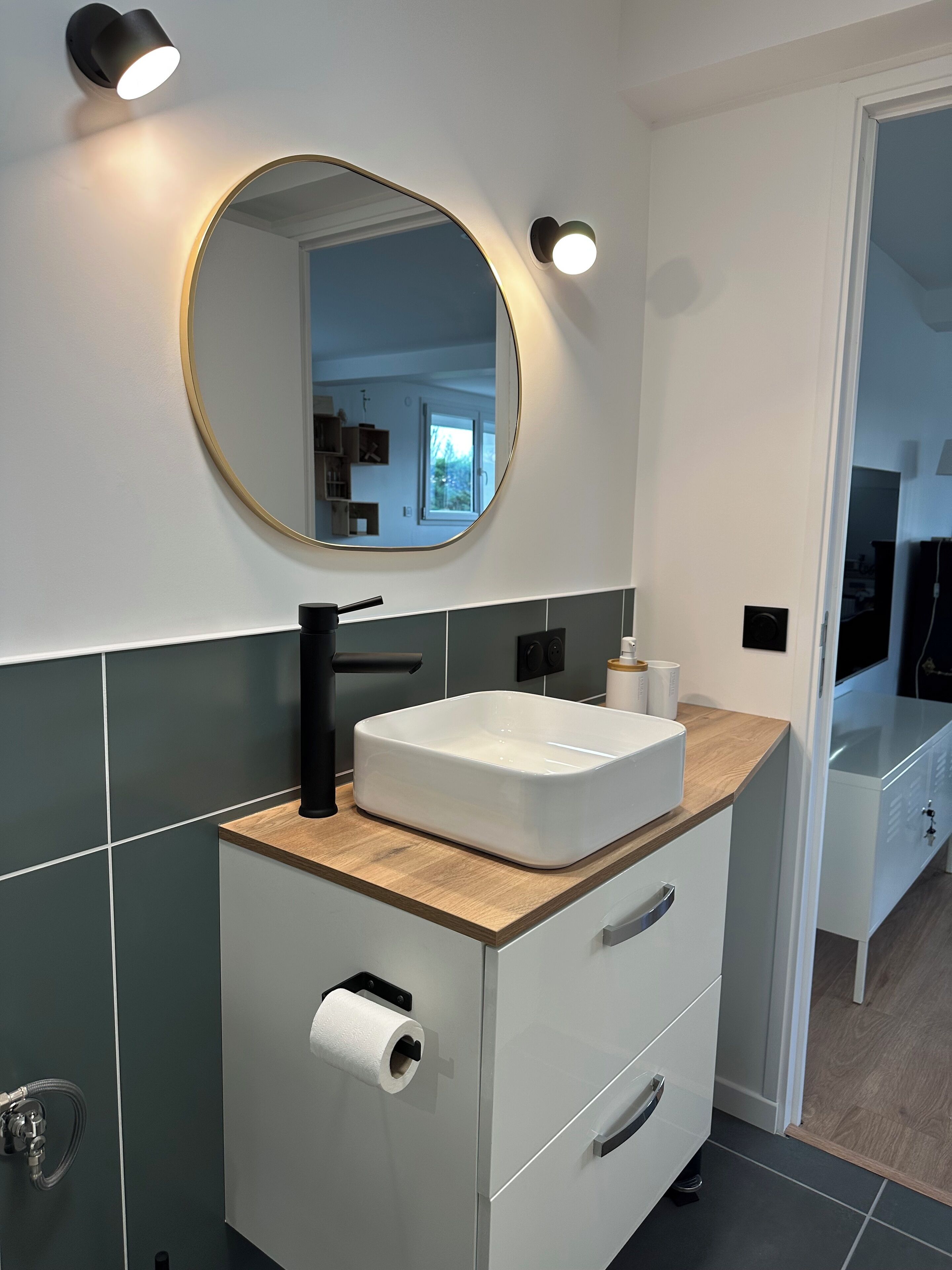 Une salle de bain moderne avec un meuble-lavabo blanc, un miroir rond et un lavabo encastré.