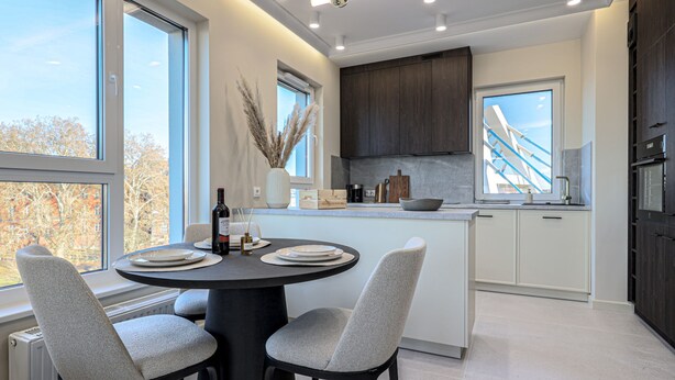 A modern kitchen with a central island, white cabinetry, and a large window offering a view of the outdoors. - Crema Centrum Bydgoszczy Widok na Brd Gara (Bydgoszcz)