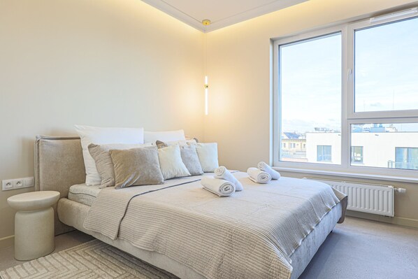 Un dormitorio con cama, mesita de noche y ventana con vistas a edificios.
