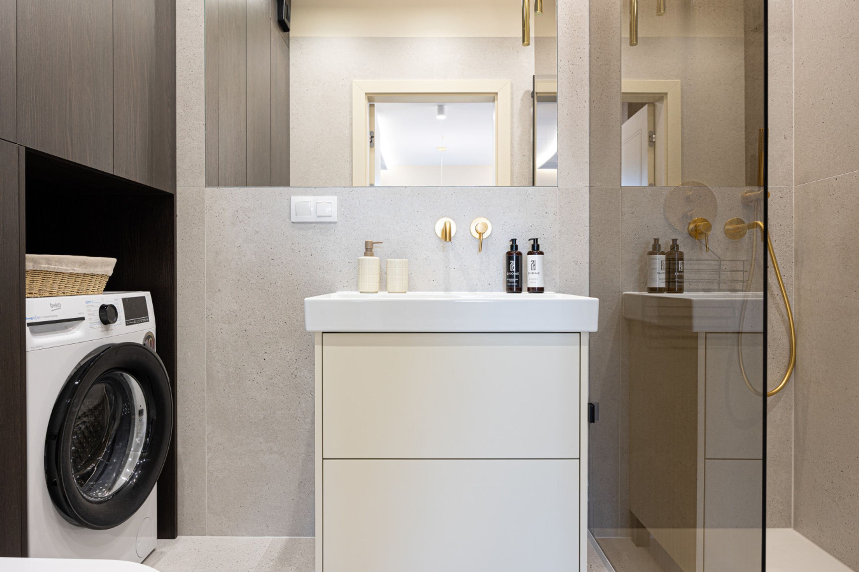 A modern bathroom with a washing machine, a sink with toiletries, and a shower with a gold showerhead.