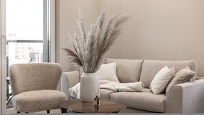 A modern living room with a beige sofa, a matching armchair, and a round coffee table. A tall vase with pampas grass is placed on the coffee table. - Crema Centrum Bydgoszczy Widok na Brd Gara (Bydgoszcz)