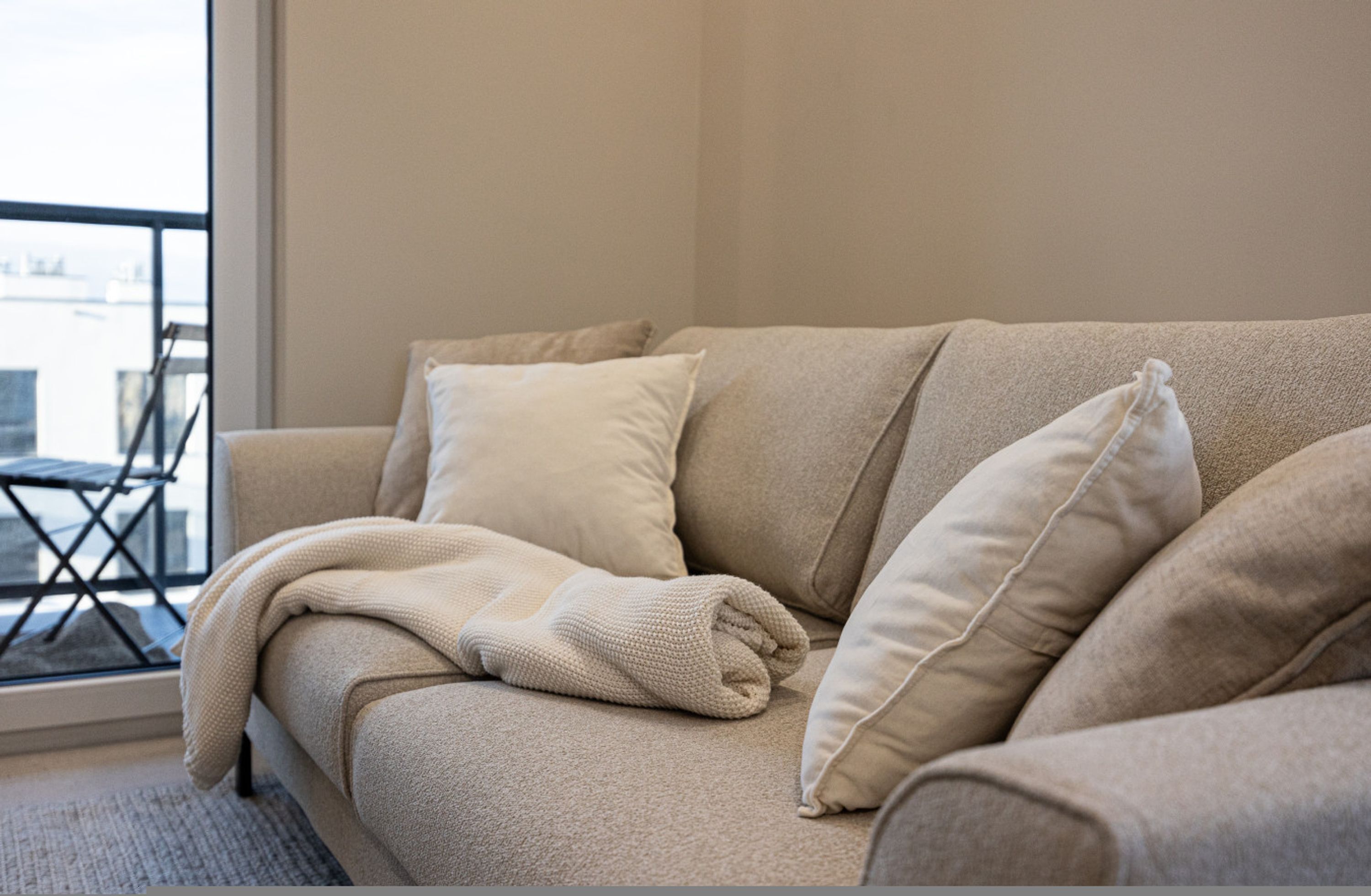 Un sofá color beige con una manta y almohadas, una mesita y vistas a un balcón.