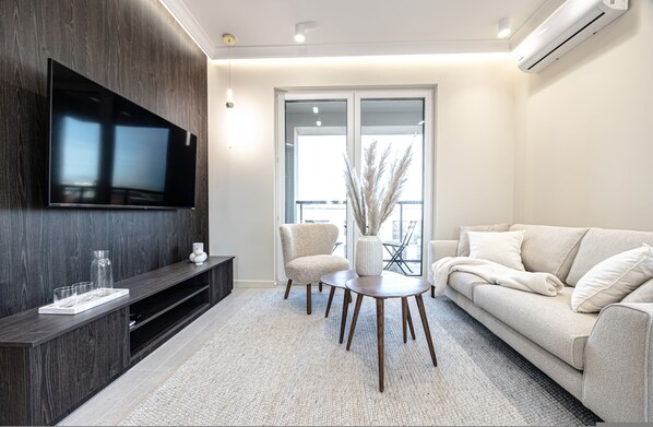 A modern living room with a flat-screen TV, a sofa, a coffee table, and a seating area with chairs.