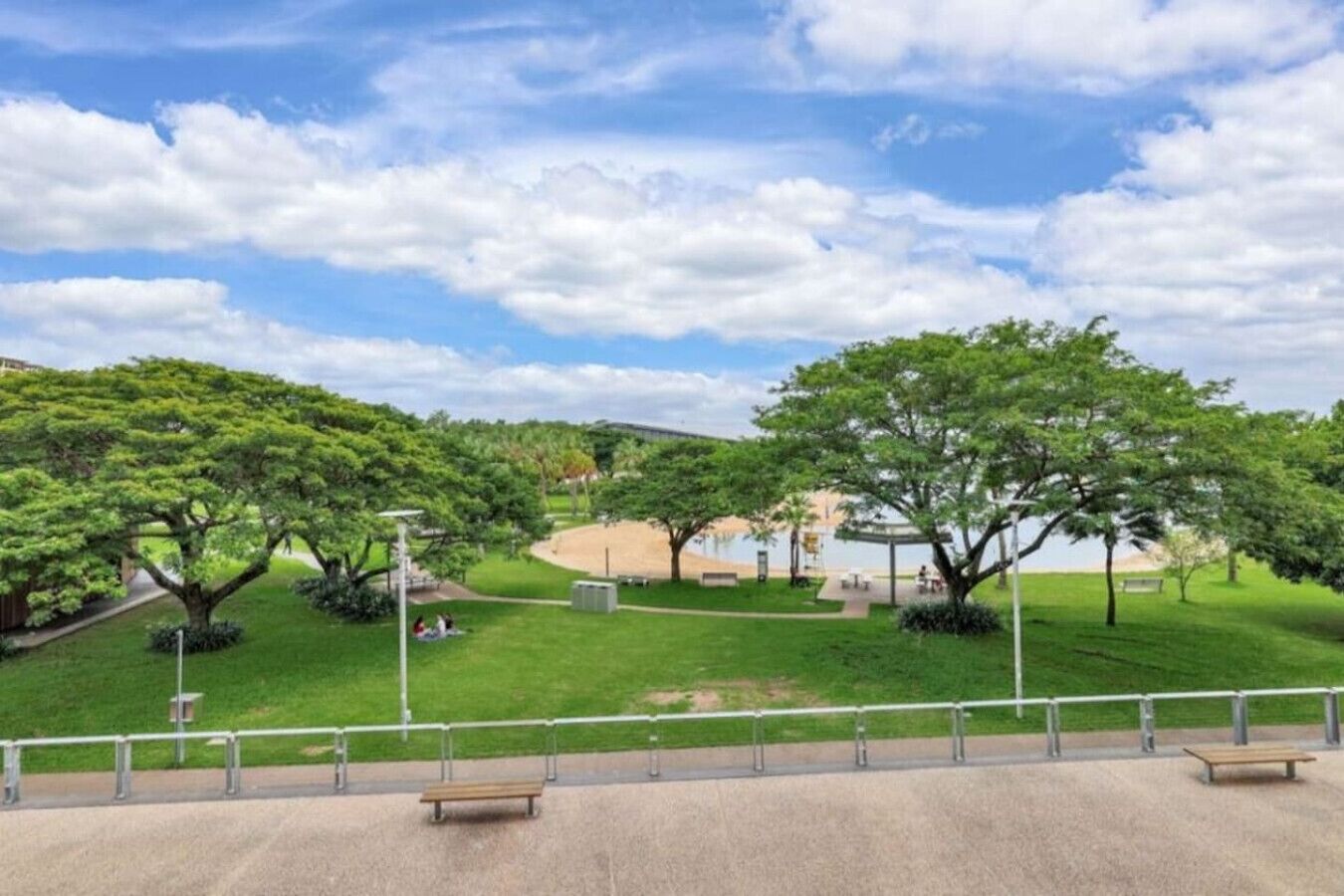 A park with a paved walkway, benches, and trees.
