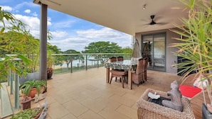 A covered outdoor patio with a table and chairs, surrounded by potted plants and a view of the sea. - Benji Zen Retreat Unique Wavepool Adults Only (Darwin)