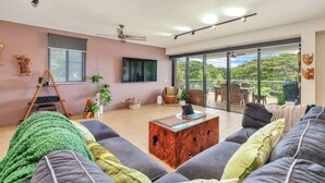 A spacious living room with a large sofa, a coffee table, and a ceiling fan. There is a sliding glass door leading to an outdoor area with a view of greenery. - Benji Zen Retreat Unique Wavepool Adults Only (Darwin)
