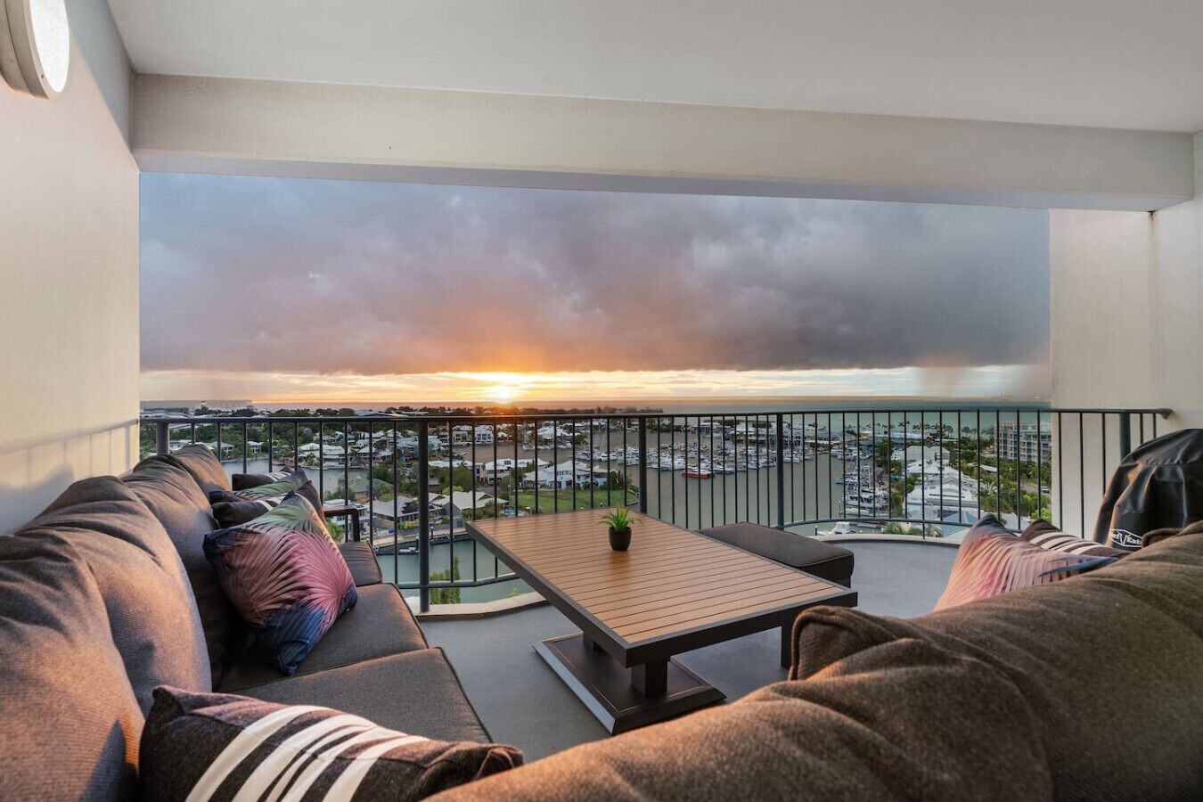 Uma varanda com sofá, uma mesa pequena e vista para um porto ao pôr do sol.