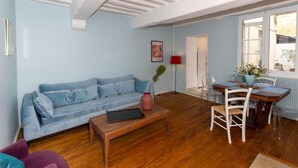 Una sala de estar con un sofá azul, una mesa de centro de madera y un comedor con una mesa y sillas de madera.