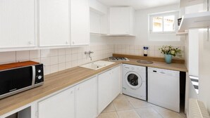 Una cocina moderna con armarios blancos, microondas, lavadora y un ventanal pequeño.