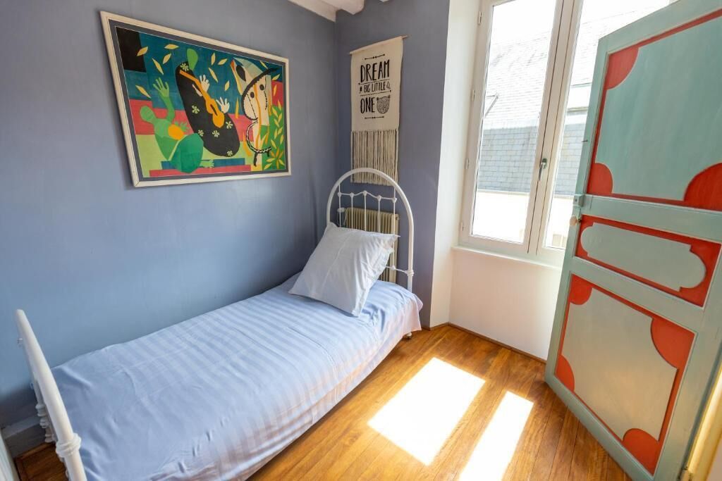 Una cama individual con estructura metálica blanca y colchón azul en una habitación con paredes azul claro.